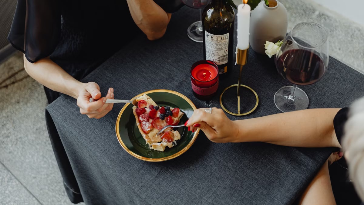 An elegant dinner setting featuring dessert, wine, and candlelight for two adults.